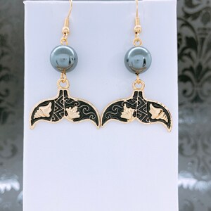 May include: Gold tone earrings with a black enamel mermaid tail design and a black pearl dangle.