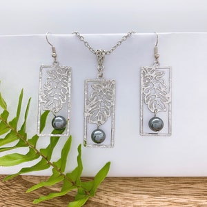May include: A silver necklace and earrings set with a leaf design and black beads. The necklace has a delicate chain and the earrings are drop style.