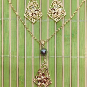 May include: A gold necklace and earrings set with a black pearl pendant. The pendant features a delicate floral design.