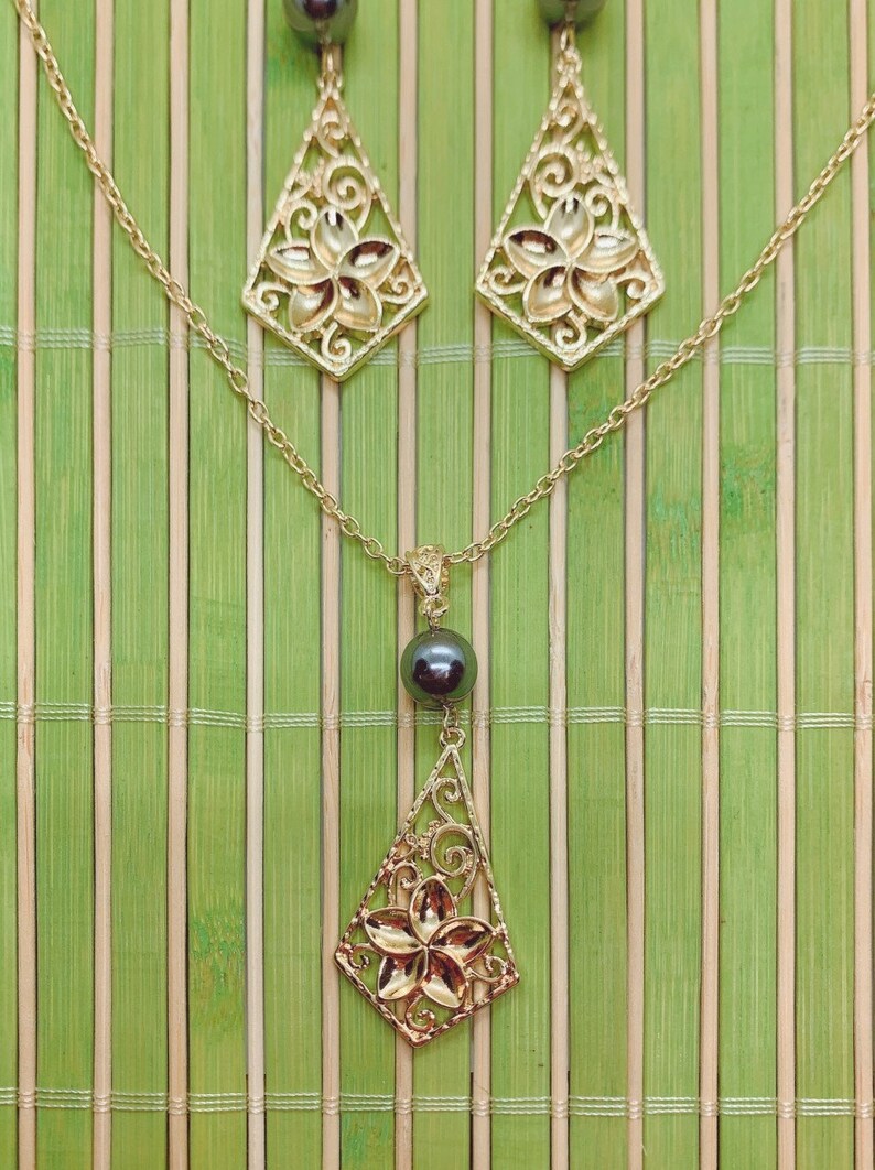 May include: A gold necklace and earrings set with a black pearl pendant. The pendant features a delicate floral design.