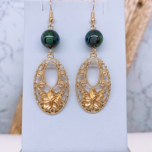 May include: Gold earrings with a black iridescent bead and a filigree design featuring a flower.