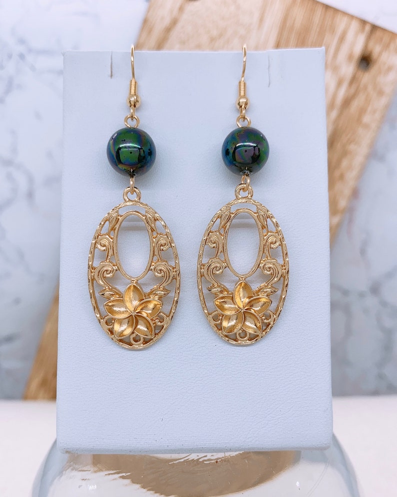 K&ouml;nnte beinhalten: Goldene Ohrringe mit einer schwarzen, schillernden Perle und einem filigranen Design mit einer Blume.