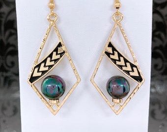May include: Gold tone earrings with a black and gold geometric design and a dark iridescent pearl drop.