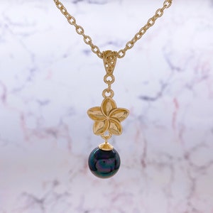 May include: A gold necklace with a plumeria flower pendant and a black pearl drop.