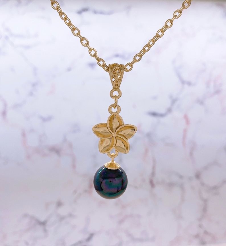 May include: A gold necklace with a plumeria flower pendant and a black pearl drop.