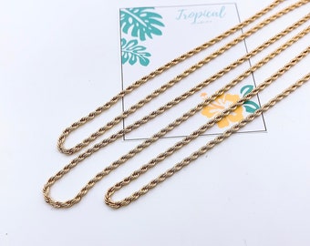 Op de afbeelding: Vier gouden touwkettingen van verschillende lengtes op een wit oppervlak. De kettingen zijn in een verspringend patroon gerangschikt, met de langste ketting bovenaan en de kortste ketting onderaan. De kettingen zijn allemaal gemaakt van een dik, gedraaid touwontwerp.