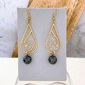 May include: Gold dangle earrings with a textured teardrop design and a black bead at the bottom.