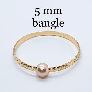 May include: A gold bangle bracelet with a 5 mm pearl charm. The bangle is engraved with a floral design.
