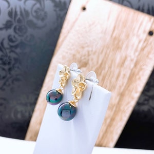 May include: A pair of gold flower earrings with black pearl drops. The earrings have a simple design and are perfect for everyday wear.