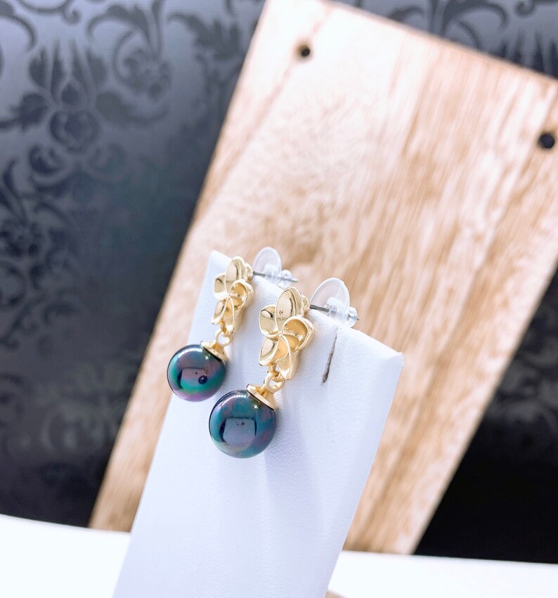 May include: A pair of gold flower earrings with black pearl drops. The earrings have a simple design and are perfect for everyday wear.