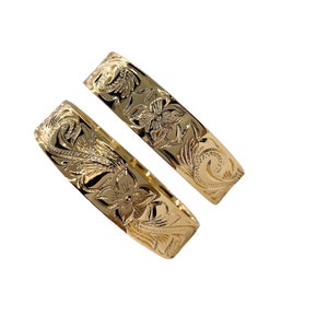 Puede incluir: Dos alianzas de boda hawaianas de oro con un dise&ntilde;o floral.