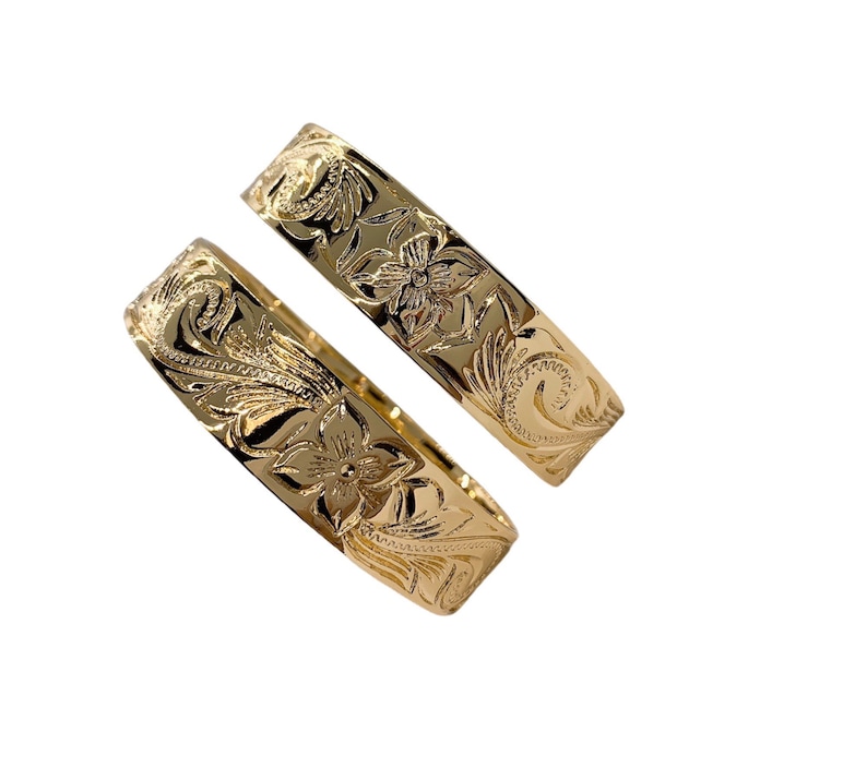 Puede incluir: Dos alianzas de boda hawaianas de oro con un dise&ntilde;o floral.