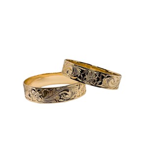 Puede incluir: Dos anillos de oro con intrincados dise&ntilde;os florales. Los anillos est&aacute;n apilados uno encima del otro.