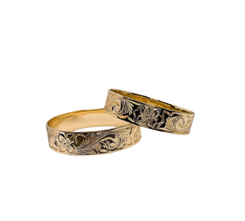 Puede incluir: Dos anillos de oro con intrincados dise&ntilde;os florales. Los anillos est&aacute;n apilados uno encima del otro.