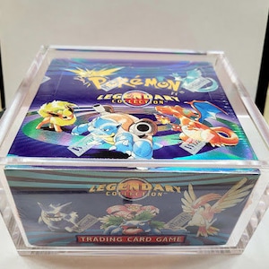 May include: A clear plastic box with a blue and purple Pokemon card inside. The card features the text "Pokemon Legendary Collection" and images of various Pokemon characters.