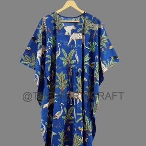 Op de afbeelding: Een blauwe katoenen kaftan met een kleurrijke print van luipaarden, zebra's en vogels in een jungle-omgeving. De kaftan heeft een V-hals en een strik in de taille.
