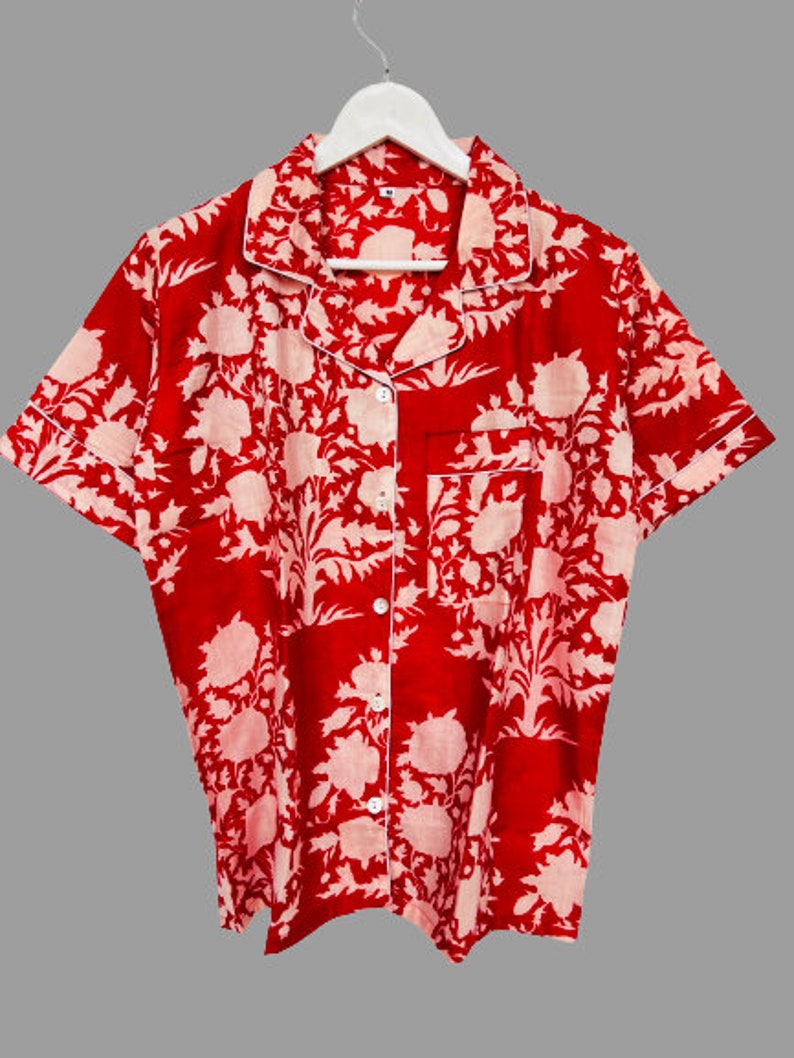 May include: Red short-sleeved button-up shirt with a white floral print. The shirt has a collared neckline and a pocket on the left chest.