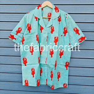 May include: Light blue pajama shirt with a red lobster print. The shirt has short sleeves, a button-down front, and white trim. The text "thefabricraft" is printed on the shirt.
