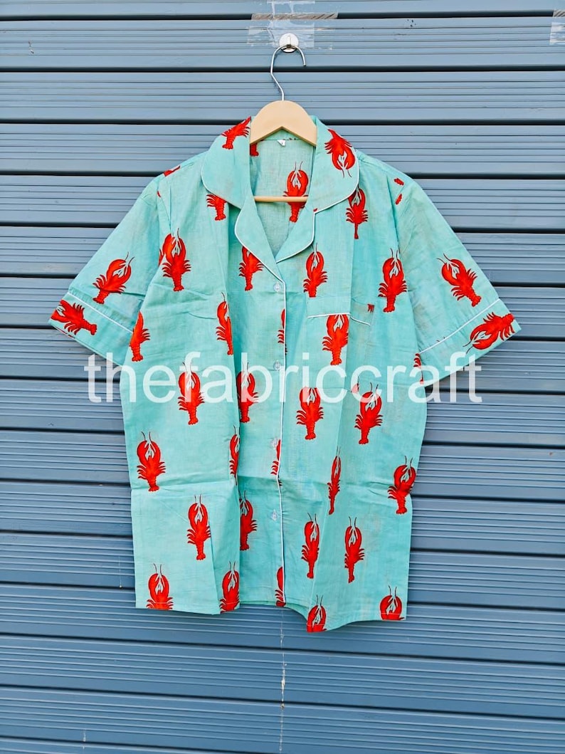 May include: Light blue pajama shirt with a red lobster print. The shirt has short sleeves, a button-down front, and white trim. The text "thefabricraft" is printed on the shirt.