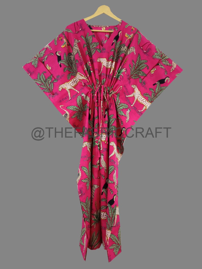 Op de afbeelding: Een roze kaftan met een jungleprint met luipaarden, toekans, zebra's en palmbomen. De kaftan heeft een V-hals en een trekkoord in de taille.