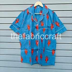 May include: Blue short-sleeved pajama top with a red lobster pattern. The top has white trim on the collar, cuffs, and pocket. The text "thefabriccraft" is printed on the front.