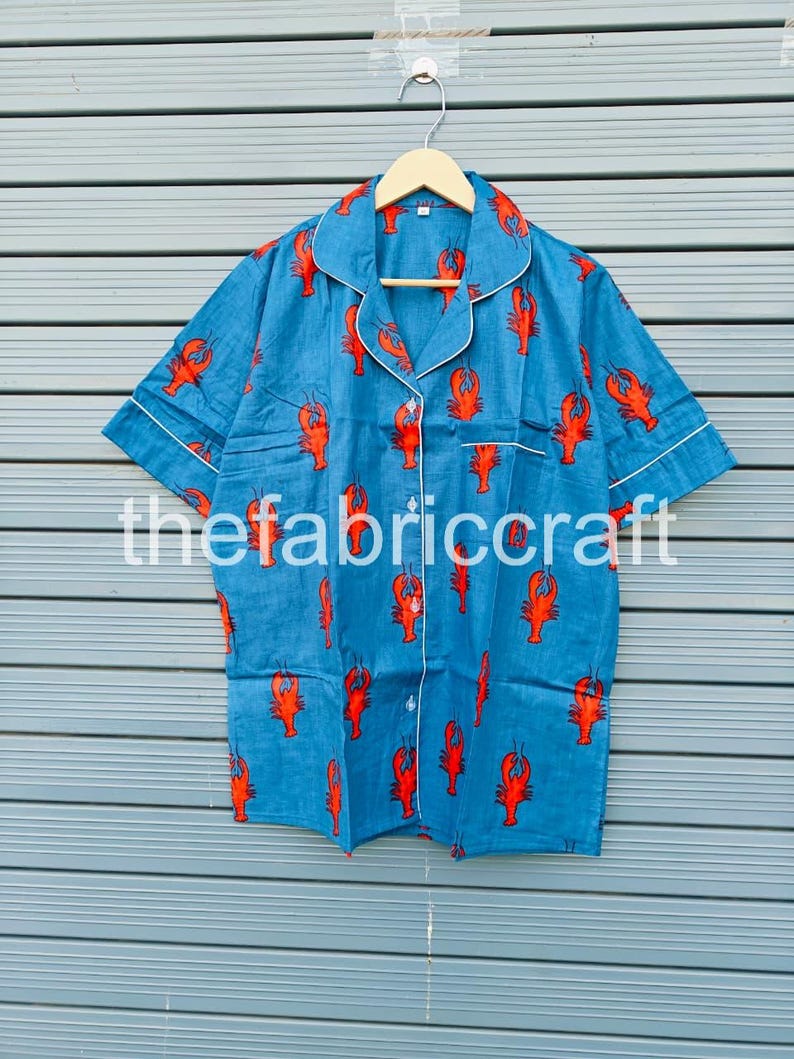 May include: Blue short-sleeved pajama top with a red lobster pattern. The top has white trim on the collar, cuffs, and pocket. The text "thefabriccraft" is printed on the front.