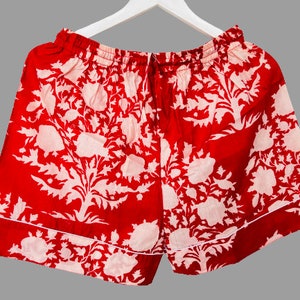 May include: Red cotton shorts with a white floral print. The shorts have a drawstring waist and a white trim.