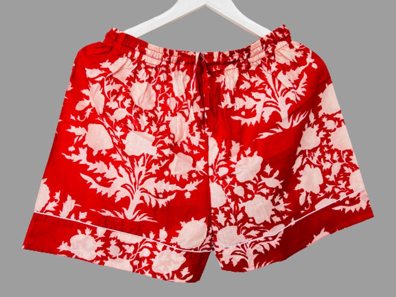 May include: Red cotton shorts with a white floral print. The shorts have a drawstring waist and a white trim.