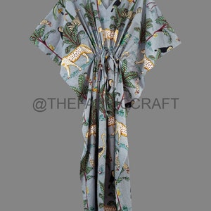 Op de afbeelding: Een lichtblauwe kaftan met een jungleprint met luipaarden, toekans en palmbomen. De kaftan heeft een trekkoord in de taille en korte mouwen.