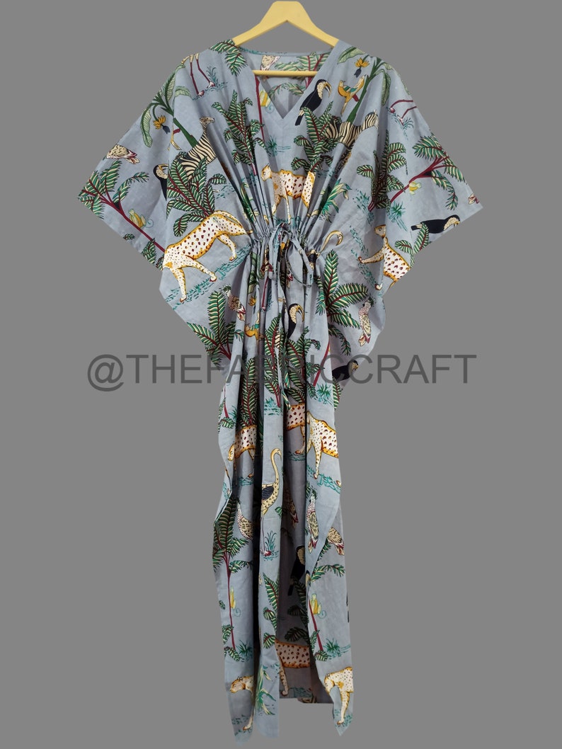 Op de afbeelding: Een lichtblauwe kaftan met een jungleprint met luipaarden, toekans en palmbomen. De kaftan heeft een trekkoord in de taille en korte mouwen.