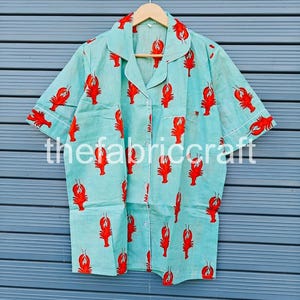 May include: Light blue pajama shirt with a red lobster print. The shirt has short sleeves, a button-down front, and white trim. The text "thefabriccraft" is printed on the shirt.