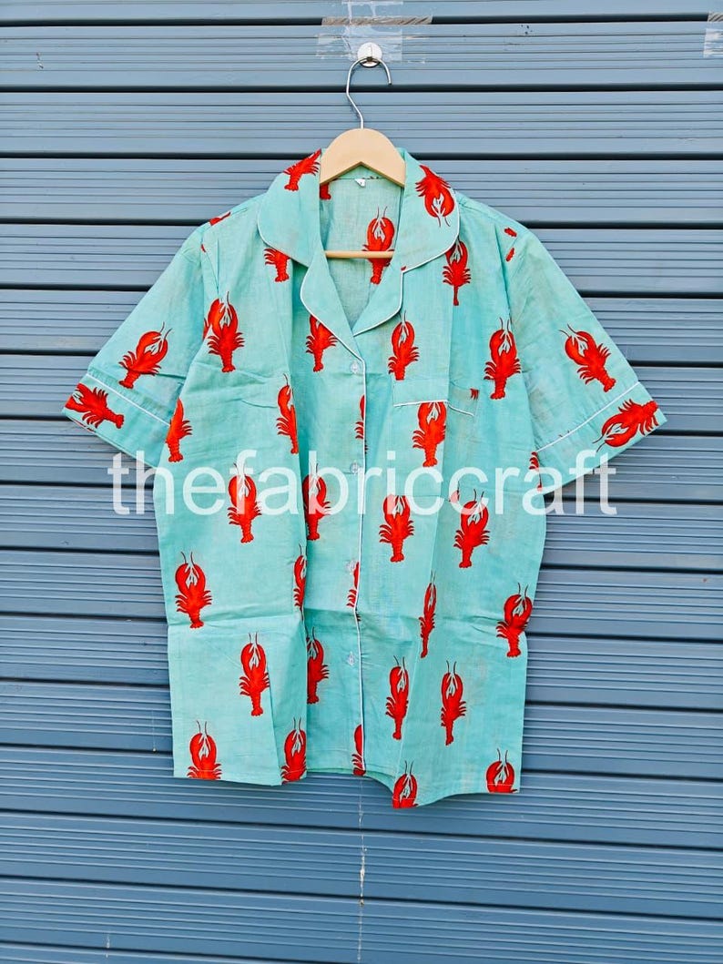 May include: Light blue pajama shirt with a red lobster print. The shirt has short sleeves, a button-down front, and white trim. The text "thefabriccraft" is printed on the shirt.