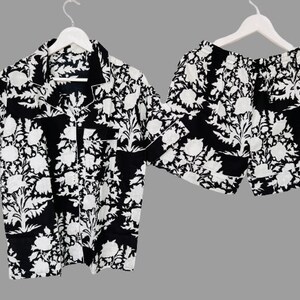 May include: A black and white patterned short-sleeved shirt and matching shorts set. The shirt has a collared neckline and a button-up front. The shorts have an elastic waistband.
