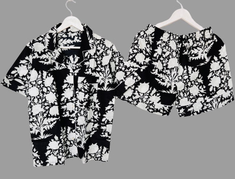 May include: A black and white patterned short-sleeved shirt and matching shorts set. The shirt has a collared neckline and a button-up front. The shorts have an elastic waistband.