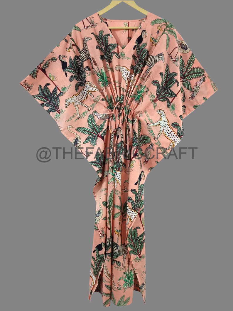 Op de afbeelding: Een perzikkleurige kaftan met een V-hals en een trekkoord in de taille. De kaftan heeft een jungleprint met zebra's, luipaarden, toekans en palmbomen. De tekst "@THEFABRICCRAFT" staat gedrukt op de onderkant van de kaftan.