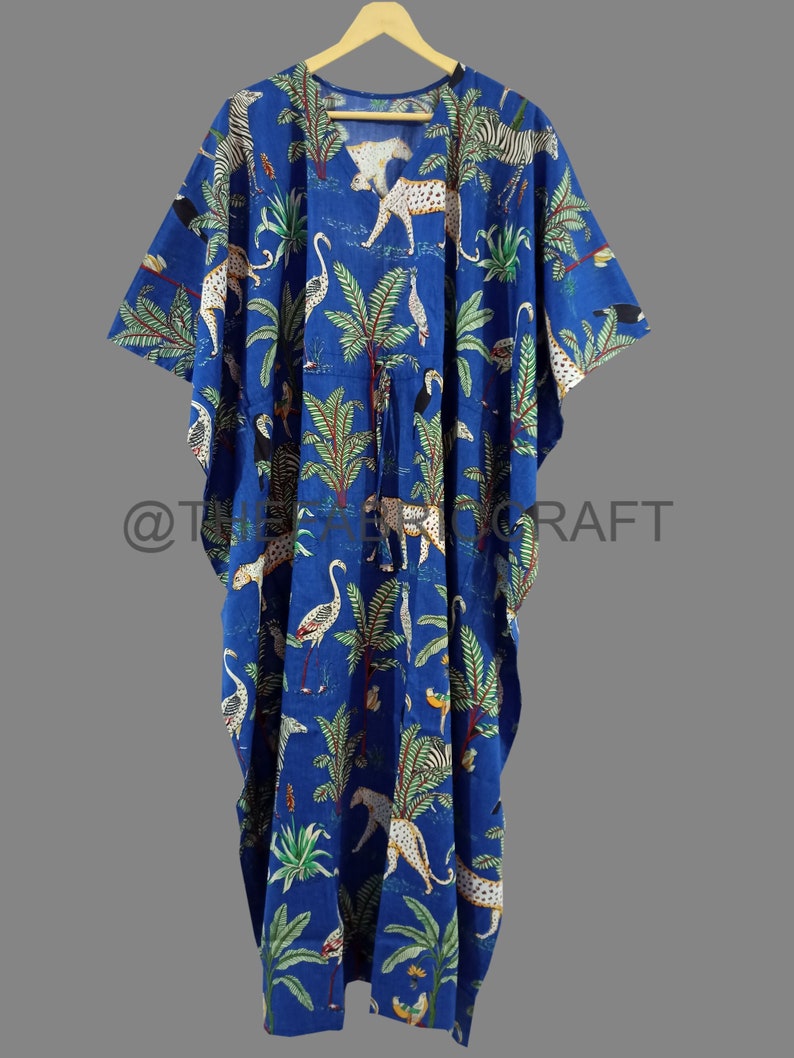 Op de afbeelding: Een blauwe katoenen kaftan met een kleurrijke print van luipaarden, zebra's en vogels in een jungle-omgeving. De kaftan heeft een V-hals en een strik in de taille.