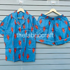 May include: Blue pajama set with a red lobster print. The set includes a short-sleeved button-down shirt and matching shorts, both trimmed with white piping. The text "thefabriccraft" is visible on the shirt.