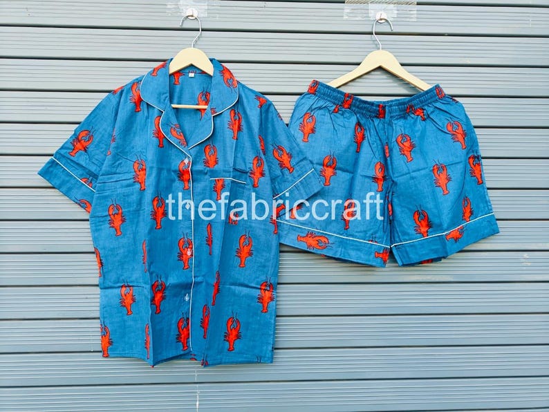 May include: Blue pajama set with a red lobster print. The set includes a short-sleeved button-down shirt and matching shorts, both trimmed with white piping. The text "thefabriccraft" is visible on the shirt.