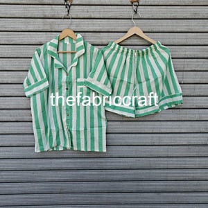 Può includere: Un pigiama a righe verdi e bianche con una camicia a maniche corte abbottonata e pantaloncini abbinati. Il testo "thefabriccraft" è visibile sulla camicia.