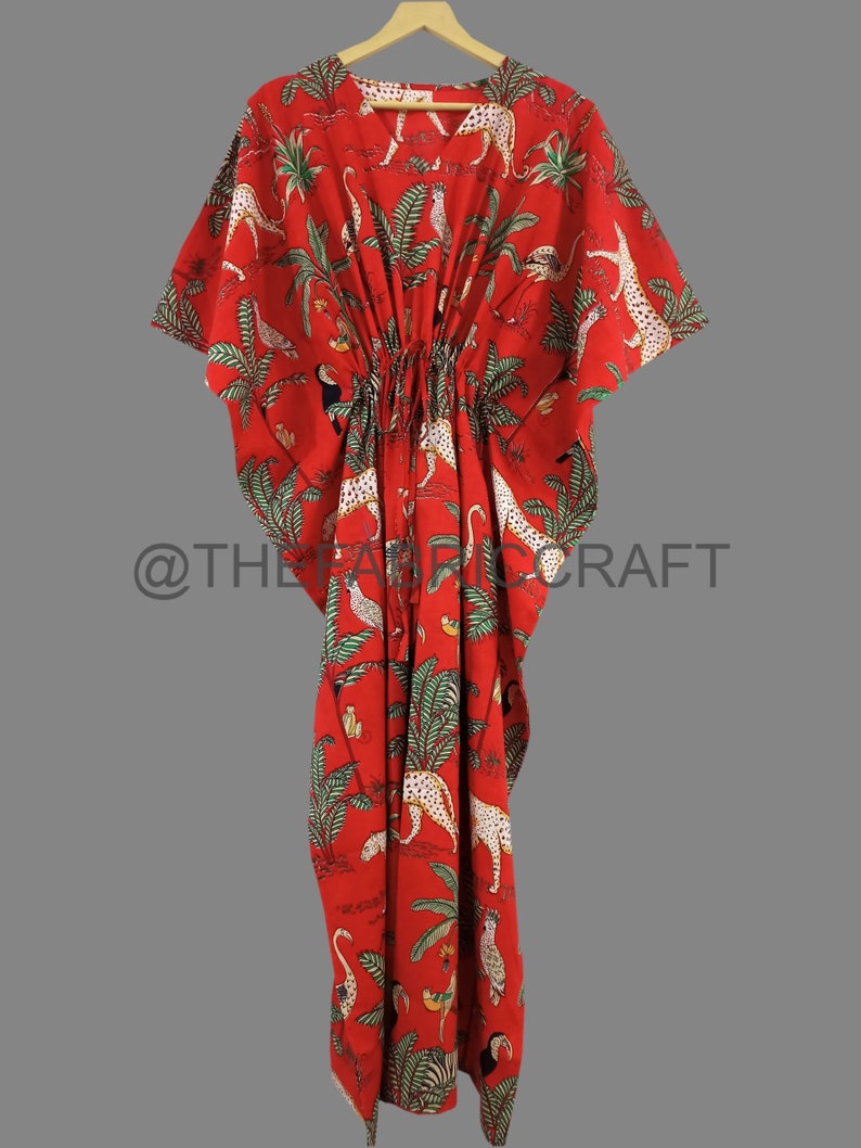 Op de afbeelding: Rode kaftan met een tropische print met luipaarden, toekans en palmbomen. De kaftan heeft een trekkoord in de taille en korte mouwen.