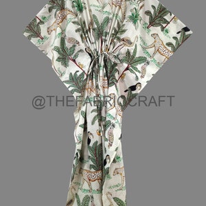 Op de afbeelding: Witte katoenen kaftan met een groene, zwarte en bruine dierenprint. De print bevat luipaarden, toekans en palmbomen. De kaftan heeft een V-hals en een tailleband.