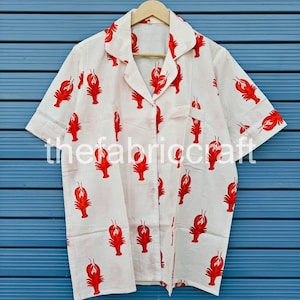 May include: White button-down shirt with short sleeves, featuring a repeating pattern of red lobsters. The shirt has a collared neckline and a breast pocket. The text "thefabriccraft" is printed on the shirt.