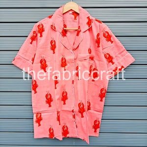 May include: A coral-colored pajama shirt with a red lobster pattern. The short-sleeved shirt has white trim and a breast pocket. The text "thefabriccraft" is printed on the shirt.