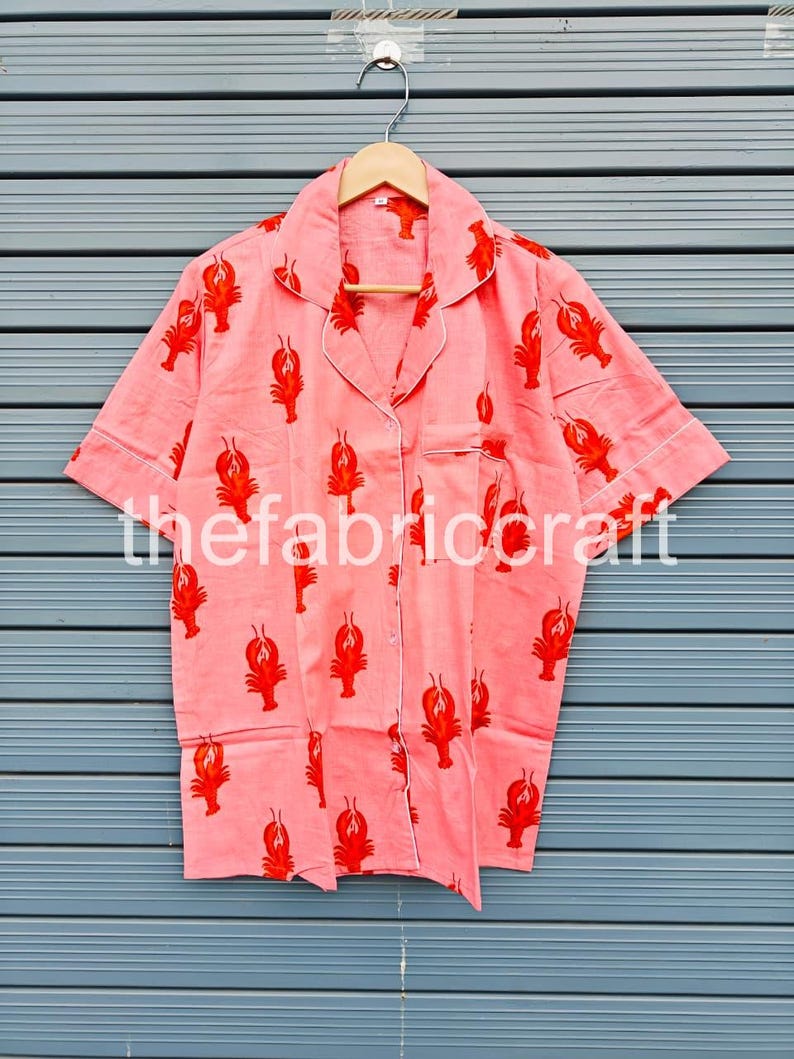 May include: A coral-colored pajama shirt with a red lobster pattern. The short-sleeved shirt has white trim and a breast pocket. The text "thefabriccraft" is printed on the shirt.