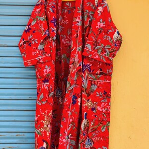 以下が含まれることがあります： 白い花柄と鳥柄の赤い綿のローブ。ローブは縁に白いトリムがあり、結び紐が付いています。