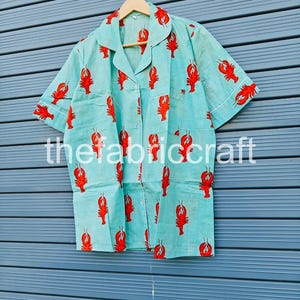 May include: Light blue pajama set with a red lobster print. The short-sleeved top and matching bottoms feature a button-down front and white trim. The text "thefabriccraft" is printed on the bottom of the image.