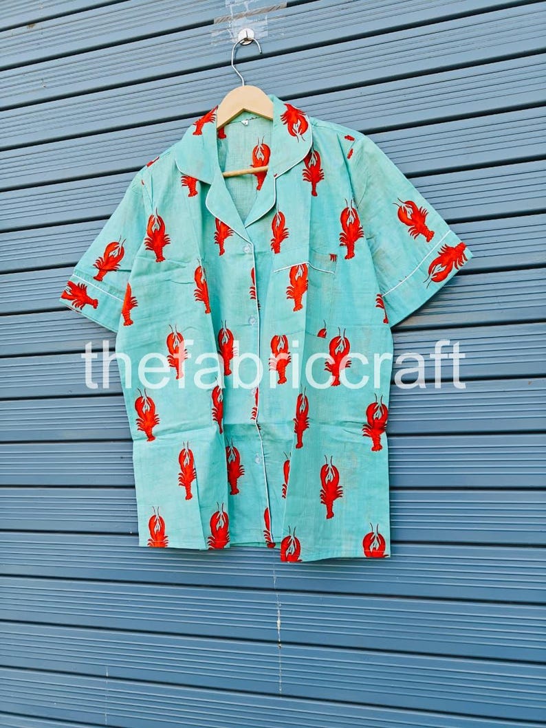 May include: Light blue pajama set with a red lobster print. The short-sleeved top and matching bottoms feature a button-down front and white trim. The text "thefabriccraft" is printed on the bottom of the image.