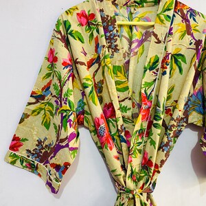 以下が含まれることがあります： カラフルな鳥と花が描かれた花柄のベージュの綿のローブ。ローブは紐ベルトと長袖です。