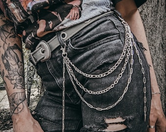 May include: A person wearing black ripped jeans with a silver chain belt and a black t-shirt with a band graphic print.