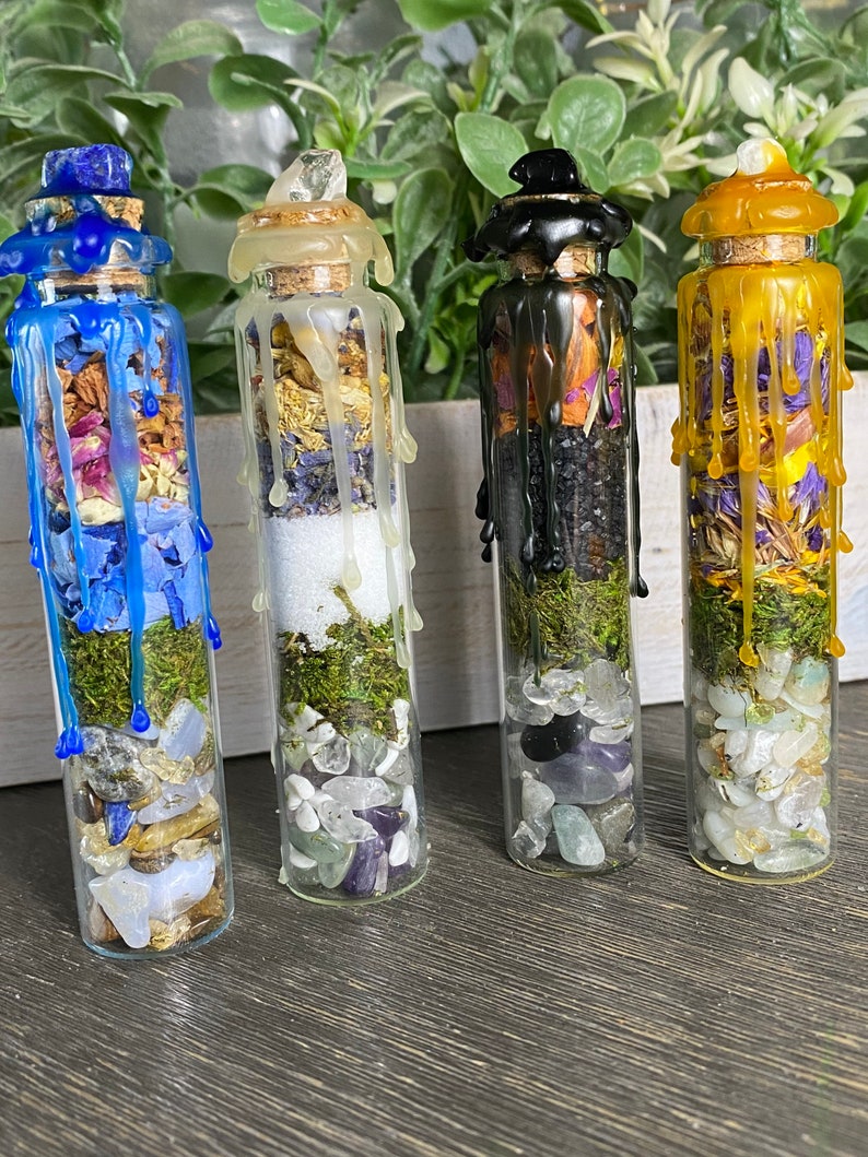 May include: Four small glass bottles filled with various crystals, herbs, and moss. Each bottle is topped with a different colored wax seal, including blue, white, black, and yellow.